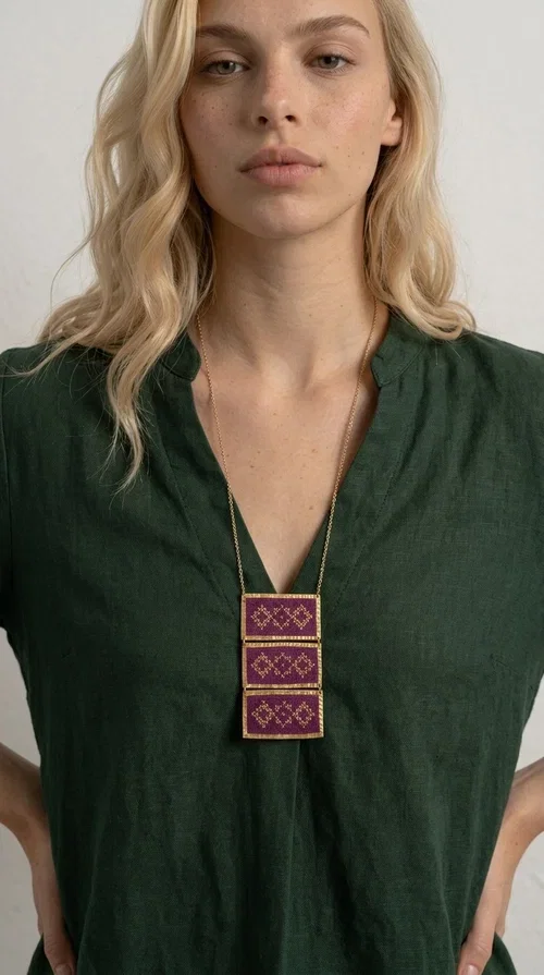 , The embroidered necklace in deep burgundy is a statement piece that instantly draws attention and transforms any outfit into something special. Designed by Greek Jewelry Designer Aikaterini Chalkiadaki, this handmade necklace combines the tradition of Greek embroidery art with a contemporary aesthetic, creating a result that is both timeless and unique.

The necklace features three rectangular fabric sections in rich burgundy, each adorned with delicate geometric patterns in gold thread — inspired by the folk tradition of Greek embroidery. The gold-toned brass frame enhances its striking presence, while the slender gold chain lends an elegant balance between bold and feminine.

Ideal for both casual and formal occasions alike, it pairs perfectly with a white t-shirt, a black dress, or even an office outfit. A perfect gift for women who love large, striking jewelry with soul and story.