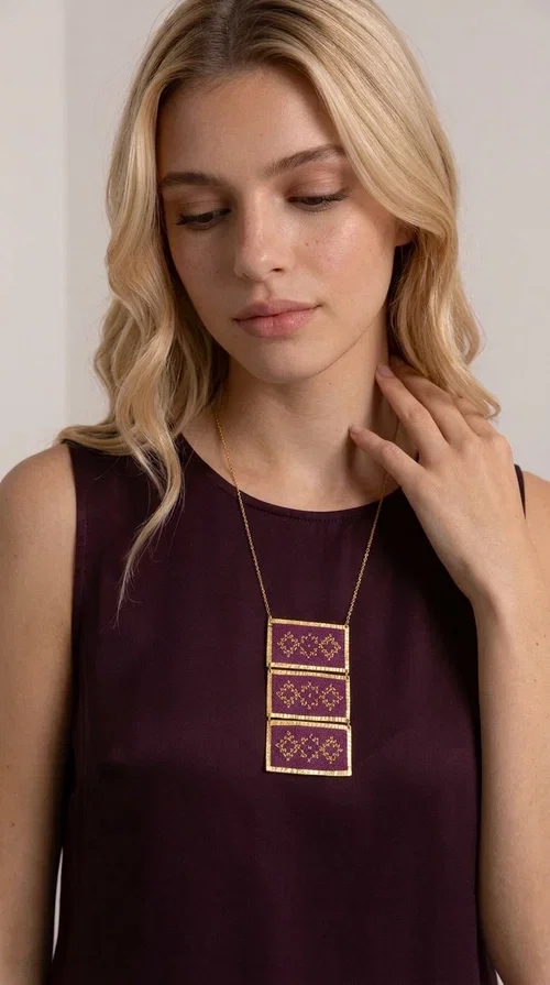 , The embroidered necklace in deep burgundy is a statement piece that instantly draws attention and transforms any outfit into something special. Designed by Greek Jewelry Designer Aikaterini Chalkiadaki, this handmade necklace combines the tradition of Greek embroidery art with a contemporary aesthetic, creating a result that is both timeless and unique.

The necklace features three rectangular fabric sections in rich burgundy, each adorned with delicate geometric patterns in gold thread — inspired by the folk tradition of Greek embroidery. The gold-toned brass frame enhances its striking presence, while the slender gold chain lends an elegant balance between bold and feminine.

Ideal for both casual and formal occasions alike, it pairs perfectly with a white t-shirt, a black dress, or even an office outfit. A perfect gift for women who love large, striking jewelry with soul and story.
