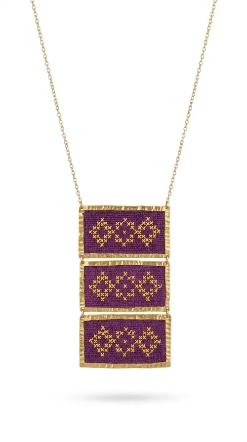 , The embroidered necklace in deep burgundy is a statement piece that instantly draws attention and transforms any outfit into something special. Designed by Greek Jewelry Designer Aikaterini Chalkiadaki, this handmade necklace combines the tradition of Greek embroidery art with a contemporary aesthetic, creating a result that is both timeless and unique.

The necklace features three rectangular fabric sections in rich burgundy, each adorned with delicate geometric patterns in gold thread — inspired by the folk tradition of Greek embroidery. The gold-toned brass frame enhances its striking presence, while the slender gold chain lends an elegant balance between bold and feminine.

Ideal for both casual and formal occasions alike, it pairs perfectly with a white t-shirt, a black dress, or even an office outfit. A perfect gift for women who love large, striking jewelry with soul and story.