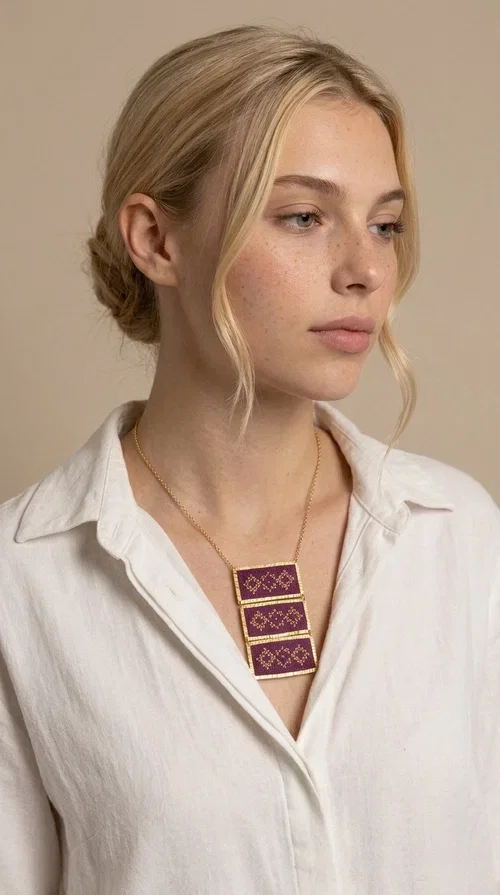 , The embroidered necklace in deep burgundy is a statement piece that instantly draws attention and transforms any outfit into something special. Designed by Greek Jewelry Designer Aikaterini Chalkiadaki, this handmade necklace combines the tradition of Greek embroidery art with a contemporary aesthetic, creating a result that is both timeless and unique.

The necklace features three rectangular fabric sections in rich burgundy, each adorned with delicate geometric patterns in gold thread — inspired by the folk tradition of Greek embroidery. The gold-toned brass frame enhances its striking presence, while the slender gold chain lends an elegant balance between bold and feminine.

Ideal for both casual and formal occasions alike, it pairs perfectly with a white t-shirt, a black dress, or even an office outfit. A perfect gift for women who love large, striking jewelry with soul and story.