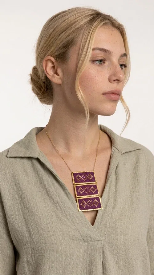 , The embroidered necklace in deep burgundy is a statement piece that instantly draws attention and transforms any outfit into something special. Designed by Greek Jewelry Designer Aikaterini Chalkiadaki, this handmade necklace combines the tradition of Greek embroidery art with a contemporary aesthetic, creating a result that is both timeless and unique.

The necklace features three rectangular fabric sections in rich burgundy, each adorned with delicate geometric patterns in gold thread — inspired by the folk tradition of Greek embroidery. The gold-toned brass frame enhances its striking presence, while the slender gold chain lends an elegant balance between bold and feminine.

Ideal for both casual and formal occasions alike, it pairs perfectly with a white t-shirt, a black dress, or even an office outfit. A perfect gift for women who love large, striking jewelry with soul and story.
