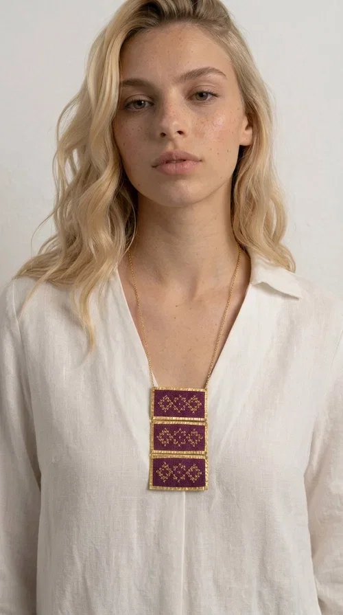 , The embroidered necklace in deep burgundy is a statement piece that instantly draws attention and transforms any outfit into something special. Designed by Greek Jewelry Designer Aikaterini Chalkiadaki, this handmade necklace combines the tradition of Greek embroidery art with a contemporary aesthetic, creating a result that is both timeless and unique.

The necklace features three rectangular fabric sections in rich burgundy, each adorned with delicate geometric patterns in gold thread — inspired by the folk tradition of Greek embroidery. The gold-toned brass frame enhances its striking presence, while the slender gold chain lends an elegant balance between bold and feminine.

Ideal for both casual and formal occasions alike, it pairs perfectly with a white t-shirt, a black dress, or even an office outfit. A perfect gift for women who love large, striking jewelry with soul and story.