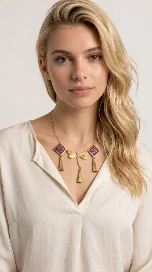 , A statement embroidered necklace that combines the traditional art of embroidery with modern aesthetics — ideal for every woman who wants to express herself with style and originality. Designed by Greek Jewelry Designer Aikaterini Chalkiadaki, this handmade necklace is a true piece of wearable art, inspired by folk heritage and the geometric motifs of Greek tradition.

The necklace features two embroidered square elements in deep burgundy color with gold geometric patterns, joined by a central gold butterfly-shaped motif made of brass. Three gold tassels hang lightly, adding movement and charm to the whole. The gold-tone brass chain completes the elegant, striking look.

It pairs perfectly over simple, solid-colored outfits — such as a blue v-neck top — instantly adding character to your look. Suitable for daytime appearances, nights out, and as a unique gift for women who love striking, feminine jewelry.