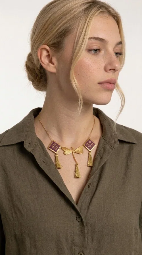 , A statement embroidered necklace that combines the traditional art of embroidery with modern aesthetics — ideal for every woman who wants to express herself with style and originality. Designed by Greek Jewelry Designer Aikaterini Chalkiadaki, this handmade necklace is a true piece of wearable art, inspired by folk heritage and the geometric motifs of Greek tradition.

The necklace features two embroidered square elements in deep burgundy color with gold geometric patterns, joined by a central gold butterfly-shaped motif made of brass. Three gold tassels hang lightly, adding movement and charm to the whole. The gold-tone brass chain completes the elegant, striking look.

It pairs perfectly over simple, solid-colored outfits — such as a blue v-neck top — instantly adding character to your look. Suitable for daytime appearances, nights out, and as a unique gift for women who love striking, feminine jewelry.