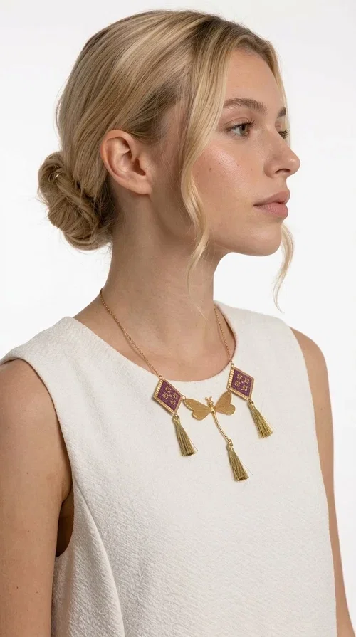 , A statement embroidered necklace that combines the traditional art of embroidery with modern aesthetics — ideal for every woman who wants to express herself with style and originality. Designed by Greek Jewelry Designer Aikaterini Chalkiadaki, this handmade necklace is a true piece of wearable art, inspired by folk heritage and the geometric motifs of Greek tradition.

The necklace features two embroidered square elements in deep burgundy color with gold geometric patterns, joined by a central gold butterfly-shaped motif made of brass. Three gold tassels hang lightly, adding movement and charm to the whole. The gold-tone brass chain completes the elegant, striking look.

It pairs perfectly over simple, solid-colored outfits — such as a blue v-neck top — instantly adding character to your look. Suitable for daytime appearances, nights out, and as a unique gift for women who love striking, feminine jewelry.