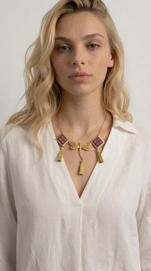 , A statement embroidered necklace that combines the traditional art of embroidery with modern aesthetics — ideal for every woman who wants to express herself with style and originality. Designed by Greek Jewelry Designer Aikaterini Chalkiadaki, this handmade necklace is a true piece of wearable art, inspired by folk heritage and the geometric motifs of Greek tradition.

The necklace features two embroidered square elements in deep burgundy color with gold geometric patterns, joined by a central gold butterfly-shaped motif made of brass. Three gold tassels hang lightly, adding movement and charm to the whole. The gold-tone brass chain completes the elegant, striking look.

It pairs perfectly over simple, solid-colored outfits — such as a blue v-neck top — instantly adding character to your look. Suitable for daytime appearances, nights out, and as a unique gift for women who love striking, feminine jewelry.