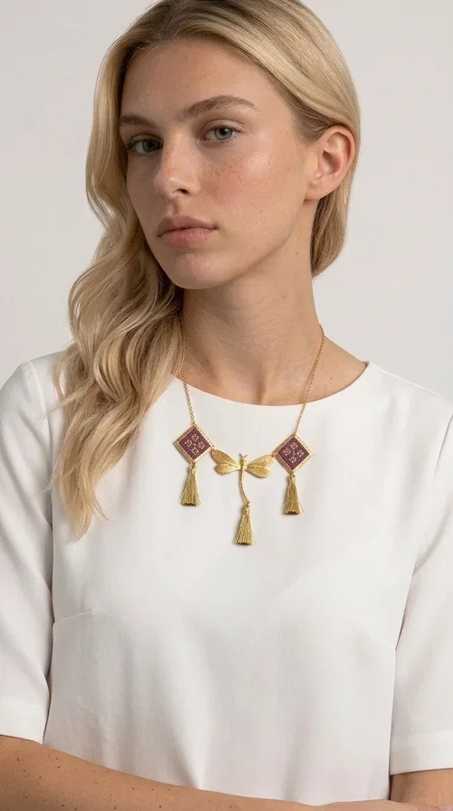 , A statement embroidered necklace that combines the traditional art of embroidery with modern aesthetics — ideal for every woman who wants to express herself with style and originality. Designed by Greek Jewelry Designer Aikaterini Chalkiadaki, this handmade necklace is a true piece of wearable art, inspired by folk heritage and the geometric motifs of Greek tradition.

The necklace features two embroidered square elements in deep burgundy color with gold geometric patterns, joined by a central gold butterfly-shaped motif made of brass. Three gold tassels hang lightly, adding movement and charm to the whole. The gold-tone brass chain completes the elegant, striking look.

It pairs perfectly over simple, solid-colored outfits — such as a blue v-neck top — instantly adding character to your look. Suitable for daytime appearances, nights out, and as a unique gift for women who love striking, feminine jewelry.