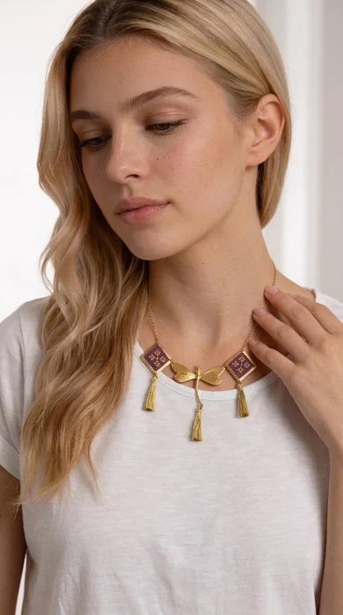 , A statement embroidered necklace that combines the traditional art of embroidery with modern aesthetics — ideal for every woman who wants to express herself with style and originality. Designed by Greek Jewelry Designer Aikaterini Chalkiadaki, this handmade necklace is a true piece of wearable art, inspired by folk heritage and the geometric motifs of Greek tradition.

The necklace features two embroidered square elements in deep burgundy color with gold geometric patterns, joined by a central gold butterfly-shaped motif made of brass. Three gold tassels hang lightly, adding movement and charm to the whole. The gold-tone brass chain completes the elegant, striking look.

It pairs perfectly over simple, solid-colored outfits — such as a blue v-neck top — instantly adding character to your look. Suitable for daytime appearances, nights out, and as a unique gift for women who love striking, feminine jewelry.