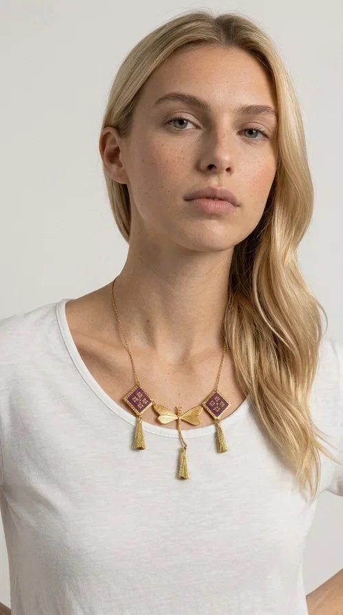 , A statement embroidered necklace that combines the traditional art of embroidery with modern aesthetics — ideal for every woman who wants to express herself with style and originality. Designed by Greek Jewelry Designer Aikaterini Chalkiadaki, this handmade necklace is a true piece of wearable art, inspired by folk heritage and the geometric motifs of Greek tradition.

The necklace features two embroidered square elements in deep burgundy color with gold geometric patterns, joined by a central gold butterfly-shaped motif made of brass. Three gold tassels hang lightly, adding movement and charm to the whole. The gold-tone brass chain completes the elegant, striking look.

It pairs perfectly over simple, solid-colored outfits — such as a blue v-neck top — instantly adding character to your look. Suitable for daytime appearances, nights out, and as a unique gift for women who love striking, feminine jewelry.
