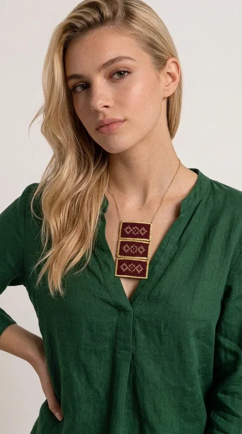 , The statement embroidered necklace in burgundy with geometric patterns is a piece of jewelry that combines the traditional art of embroidery with a modern aesthetic, creating a result that immediately catches the eye. Designed by Greek Jewelry Designer Aikaterini Chalkiadaki, this striking necklace draws inspiration from folk tradition and the geometric motifs that characterize Greek handicraft. The deep burgundy color of the fabric, combined with gold brass, creates a rich, warm palette that suits every skin tone.

The necklace consists of three rectangular embroidered sections, placed one below the other and framed with gold brass featuring a textured finish. Each section showcases handmade embroidery with repeating geometric patterns in a folklore style, reminiscent of traditional Greek embroidery. The result is a long necklace with distinctive character, ideal for elevating a simple outfit or completing a boho-chic look.