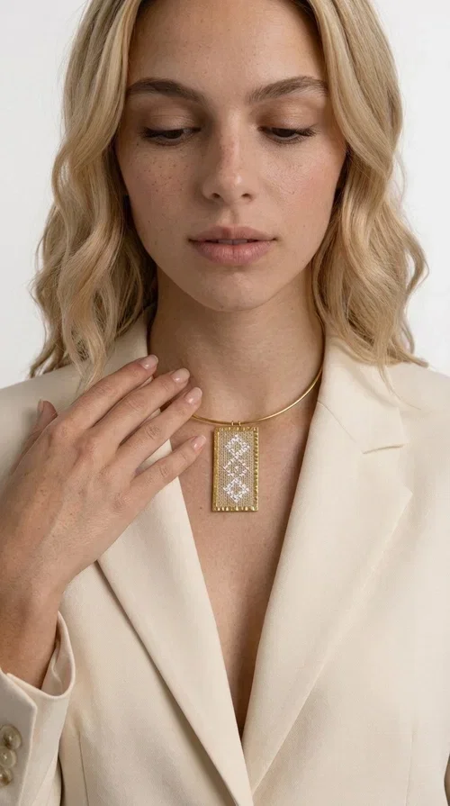 , A statement embroidered necklace that instantly catches the eye — featuring geometric patterns in cream tones and an aesthetic that blends folk tradition with contemporary style. Designed by Greek Jewelry Designer Aikaterini Chalkiadaki, this handmade piece is a distinctive choice for those seeking something beyond the ordinary.

The rectangular embroidered pendant in cream-gold tones is crafted from brass and fabric, featuring dense embroidery in geometric motifs reminiscent of folklore aesthetics. It hangs from a delicate gold-toned choker-torque style chain that elegantly and strikingly highlights the neckline. The extensive decoration with small shimmering elements adds richness and depth to the overall composition.

Ideal for casual chic or smart casual looks, it pairs beautifully with a white T-shirt, a blazer, or a summer dress. It also makes an excellent gift idea for women who appreciate handmade jewelry with a distinctive character.