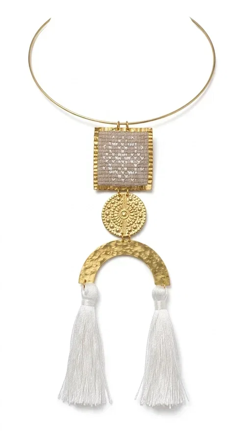 , A statement embroidered necklace that combines folk aesthetics with modern elegance — the ideal piece for those who love style with character.

Designed by Greek Jewelry Designer Aikaterini Chalkiadaki, this handmade necklace consists of three main elements: a rectangular embroidered pendant with geometric patterns in cream tones, a gold circular disc with embossed decoration, and a semicircular gold base adorned with white fabric fringes. The necklace is worn on a gold stainless steel omega chain that fits comfortably around the neck, adding balance to the striking pendant.

The materials used — brass and fabric — create a unique result that resembles a work of art. The geometric embroidered patterns are reminiscent of traditional Greek techniques, while the overall composition has a distinctly contemporary character. Ideal for casual chic looks as well as evening outings, it pairs perfectly with a white t-shirt, an oversized jacket, or a simple dress.