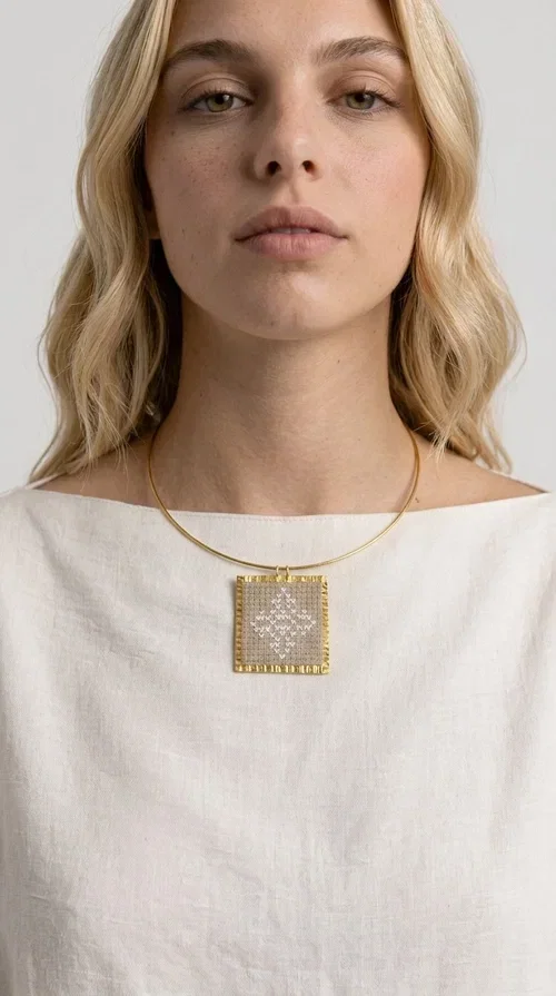 , An embroidered necklace that blends tradition with contemporary design — the Statement necklace KOL-4728 is the ideal choice for every woman who wants to express herself through unique jewelry. Designed by Greek Jewelry Designer Aikaterini Chalkiadaki, this striking necklace showcases the charm of craftsmanship in a completely modern way.

The square pendant in gold brass features delicate embroidery in a cream shade, with geometric patterns inspired by Greek folk tradition. The texture of the fabric combined with the metal frame creates a contrast that immediately catches the eye. The necklace hangs from a slender gold ring that elevates any outfit.

Ideal as a statement necklace for casual looks as well as more formal occasions, it pairs perfectly with a white t-shirt, blazer, or boho dress. It offers a boho-chic result with folklore aesthetic references, making it stand out among women's necklaces.