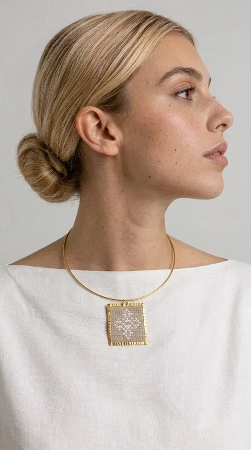 , An embroidered necklace that blends tradition with contemporary design — the Statement necklace KOL-4728 is the ideal choice for every woman who wants to express herself through unique jewelry. Designed by Greek Jewelry Designer Aikaterini Chalkiadaki, this striking necklace showcases the charm of craftsmanship in a completely modern way.

The square pendant in gold brass features delicate embroidery in a cream shade, with geometric patterns inspired by Greek folk tradition. The texture of the fabric combined with the metal frame creates a contrast that immediately catches the eye. The necklace hangs from a slender gold ring that elevates any outfit.

Ideal as a statement necklace for casual looks as well as more formal occasions, it pairs perfectly with a white t-shirt, blazer, or boho dress. It offers a boho-chic result with folklore aesthetic references, making it stand out among women's necklaces.