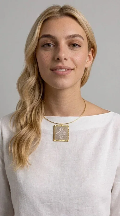 , An embroidered necklace that blends tradition with contemporary design — the Statement necklace KOL-4728 is the ideal choice for every woman who wants to express herself through unique jewelry. Designed by Greek Jewelry Designer Aikaterini Chalkiadaki, this striking necklace showcases the charm of craftsmanship in a completely modern way.

The square pendant in gold brass features delicate embroidery in a cream shade, with geometric patterns inspired by Greek folk tradition. The texture of the fabric combined with the metal frame creates a contrast that immediately catches the eye. The necklace hangs from a slender gold ring that elevates any outfit.

Ideal as a statement necklace for casual looks as well as more formal occasions, it pairs perfectly with a white t-shirt, blazer, or boho dress. It offers a boho-chic result with folklore aesthetic references, making it stand out among women's necklaces.