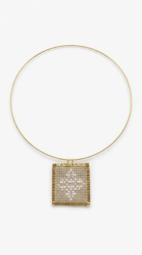 , An embroidered necklace that blends tradition with contemporary design — the Statement necklace KOL-4728 is the ideal choice for every woman who wants to express herself through unique jewelry. Designed by Greek Jewelry Designer Aikaterini Chalkiadaki, this striking necklace showcases the charm of craftsmanship in a completely modern way.

The square pendant in gold brass features delicate embroidery in a cream shade, with geometric patterns inspired by Greek folk tradition. The texture of the fabric combined with the metal frame creates a contrast that immediately catches the eye. The necklace hangs from a slender gold ring that elevates any outfit.

Ideal as a statement necklace for casual looks as well as more formal occasions, it pairs perfectly with a white t-shirt, blazer, or boho dress. It offers a boho-chic result with folklore aesthetic references, making it stand out among women's necklaces.