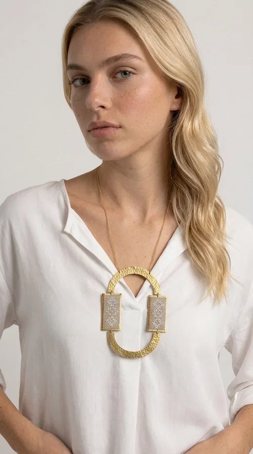 , A statement embroidered necklace that instantly catches the eye — featuring geometric patterns in an ecru shade combined with gold-toned brass that highlights its uniqueness. Designed by Greek Jewelry Designer Aikaterini Chalkiadaki, this handmade necklace blends the tradition of embroidery art with a modern, striking aesthetic result.

The ecru-colored embroidered fabric is set within two rectangular gold-toned brass frames, connected through a large oval element — creating a geometric composition full of character. The necklace hangs from a delicate gold chain, positioning the pendant right at the center of the chest for maximum visual impact. Ideal as a long statement necklace for casual or formal looks.

It pairs perfectly with simple dresses, pant-and-top sets, or low-cut tops that let the jewelry speak for itself. A perfect gift for loved ones who appreciate handmade, one-of-a-kind jewelry.