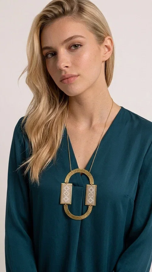 , A statement embroidered necklace that instantly catches the eye — featuring geometric patterns in an ecru shade combined with gold-toned brass that highlights its uniqueness. Designed by Greek Jewelry Designer Aikaterini Chalkiadaki, this handmade necklace blends the tradition of embroidery art with a modern, striking aesthetic result.

The ecru-colored embroidered fabric is set within two rectangular gold-toned brass frames, connected through a large oval element — creating a geometric composition full of character. The necklace hangs from a delicate gold chain, positioning the pendant right at the center of the chest for maximum visual impact. Ideal as a long statement necklace for casual or formal looks.

It pairs perfectly with simple dresses, pant-and-top sets, or low-cut tops that let the jewelry speak for itself. A perfect gift for loved ones who appreciate handmade, one-of-a-kind jewelry.