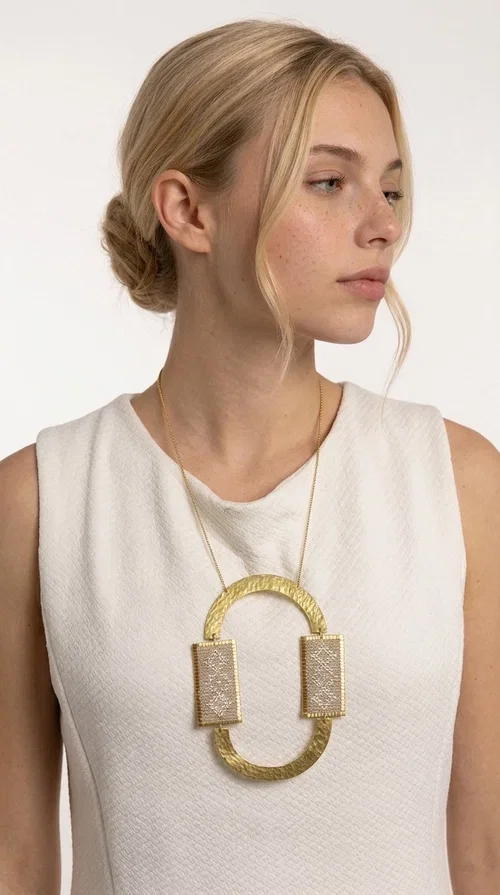 , A statement embroidered necklace that instantly catches the eye — featuring geometric patterns in an ecru shade combined with gold-toned brass that highlights its uniqueness. Designed by Greek Jewelry Designer Aikaterini Chalkiadaki, this handmade necklace blends the tradition of embroidery art with a modern, striking aesthetic result.

The ecru-colored embroidered fabric is set within two rectangular gold-toned brass frames, connected through a large oval element — creating a geometric composition full of character. The necklace hangs from a delicate gold chain, positioning the pendant right at the center of the chest for maximum visual impact. Ideal as a long statement necklace for casual or formal looks.

It pairs perfectly with simple dresses, pant-and-top sets, or low-cut tops that let the jewelry speak for itself. A perfect gift for loved ones who appreciate handmade, one-of-a-kind jewelry.