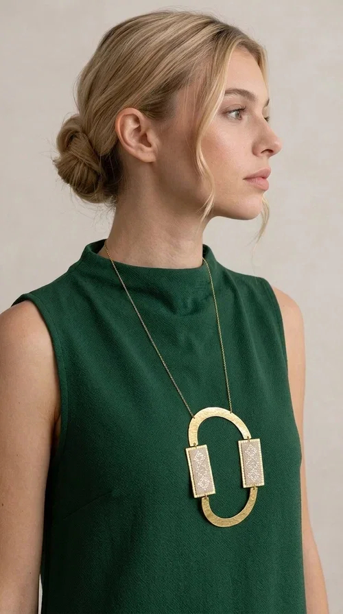 , A statement embroidered necklace that instantly catches the eye — featuring geometric patterns in an ecru shade combined with gold-toned brass that highlights its uniqueness. Designed by Greek Jewelry Designer Aikaterini Chalkiadaki, this handmade necklace blends the tradition of embroidery art with a modern, striking aesthetic result.

The ecru-colored embroidered fabric is set within two rectangular gold-toned brass frames, connected through a large oval element — creating a geometric composition full of character. The necklace hangs from a delicate gold chain, positioning the pendant right at the center of the chest for maximum visual impact. Ideal as a long statement necklace for casual or formal looks.

It pairs perfectly with simple dresses, pant-and-top sets, or low-cut tops that let the jewelry speak for itself. A perfect gift for loved ones who appreciate handmade, one-of-a-kind jewelry.