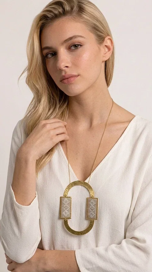 , A statement embroidered necklace that instantly catches the eye — featuring geometric patterns in an ecru shade combined with gold-toned brass that highlights its uniqueness. Designed by Greek Jewelry Designer Aikaterini Chalkiadaki, this handmade necklace blends the tradition of embroidery art with a modern, striking aesthetic result.

The ecru-colored embroidered fabric is set within two rectangular gold-toned brass frames, connected through a large oval element — creating a geometric composition full of character. The necklace hangs from a delicate gold chain, positioning the pendant right at the center of the chest for maximum visual impact. Ideal as a long statement necklace for casual or formal looks.

It pairs perfectly with simple dresses, pant-and-top sets, or low-cut tops that let the jewelry speak for itself. A perfect gift for loved ones who appreciate handmade, one-of-a-kind jewelry.