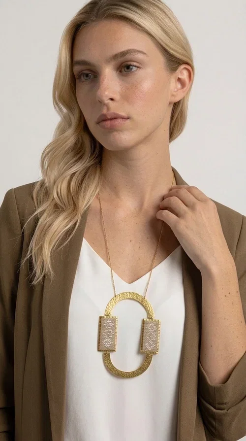 , A statement embroidered necklace that instantly catches the eye — featuring geometric patterns in an ecru shade combined with gold-toned brass that highlights its uniqueness. Designed by Greek Jewelry Designer Aikaterini Chalkiadaki, this handmade necklace blends the tradition of embroidery art with a modern, striking aesthetic result.

The ecru-colored embroidered fabric is set within two rectangular gold-toned brass frames, connected through a large oval element — creating a geometric composition full of character. The necklace hangs from a delicate gold chain, positioning the pendant right at the center of the chest for maximum visual impact. Ideal as a long statement necklace for casual or formal looks.

It pairs perfectly with simple dresses, pant-and-top sets, or low-cut tops that let the jewelry speak for itself. A perfect gift for loved ones who appreciate handmade, one-of-a-kind jewelry.