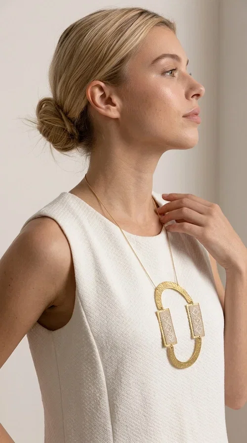 , A statement embroidered necklace that instantly catches the eye — featuring geometric patterns in an ecru shade combined with gold-toned brass that highlights its uniqueness. Designed by Greek Jewelry Designer Aikaterini Chalkiadaki, this handmade necklace blends the tradition of embroidery art with a modern, striking aesthetic result.

The ecru-colored embroidered fabric is set within two rectangular gold-toned brass frames, connected through a large oval element — creating a geometric composition full of character. The necklace hangs from a delicate gold chain, positioning the pendant right at the center of the chest for maximum visual impact. Ideal as a long statement necklace for casual or formal looks.

It pairs perfectly with simple dresses, pant-and-top sets, or low-cut tops that let the jewelry speak for itself. A perfect gift for loved ones who appreciate handmade, one-of-a-kind jewelry.