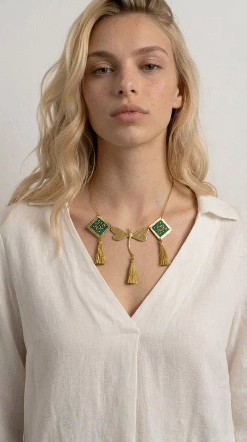 , A statement embroidered necklace that doesn't go unnoticed — featuring geometric patterns inspired by Greek tradition and a contemporary aesthetic that suits every strong feminine presence.

Designed by Greek Jewelry Designer Aikaterini Chalkiadaki, this handmade necklace combines brass and fabric in a composition strongly reminiscent of traditional folk embroidery art. Two diamond shapes of green embroidered fabric with gold geometric motifs frame a gold dragonfly at the center, while three gold tassels add movement and grace to the overall design. The result is a piece of jewelry with a deeply folklore aesthetic and, at the same time, a distinctly modern character.

Ideal for women who love striking jewelry that tells a story. It pairs perfectly with simple, monochrome looks — such as a white or cream shirt — highlighting its color and patterns. Suitable for both daytime and evening looks, receptions, weddings, or trips where you want to stand out.