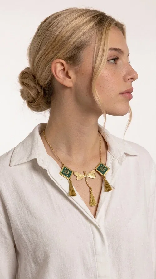 , A statement embroidered necklace that doesn't go unnoticed — featuring geometric patterns inspired by Greek tradition and a contemporary aesthetic that suits every strong feminine presence.

Designed by Greek Jewelry Designer Aikaterini Chalkiadaki, this handmade necklace combines brass and fabric in a composition strongly reminiscent of traditional folk embroidery art. Two diamond shapes of green embroidered fabric with gold geometric motifs frame a gold dragonfly at the center, while three gold tassels add movement and grace to the overall design. The result is a piece of jewelry with a deeply folklore aesthetic and, at the same time, a distinctly modern character.

Ideal for women who love striking jewelry that tells a story. It pairs perfectly with simple, monochrome looks — such as a white or cream shirt — highlighting its color and patterns. Suitable for both daytime and evening looks, receptions, weddings, or trips where you want to stand out.