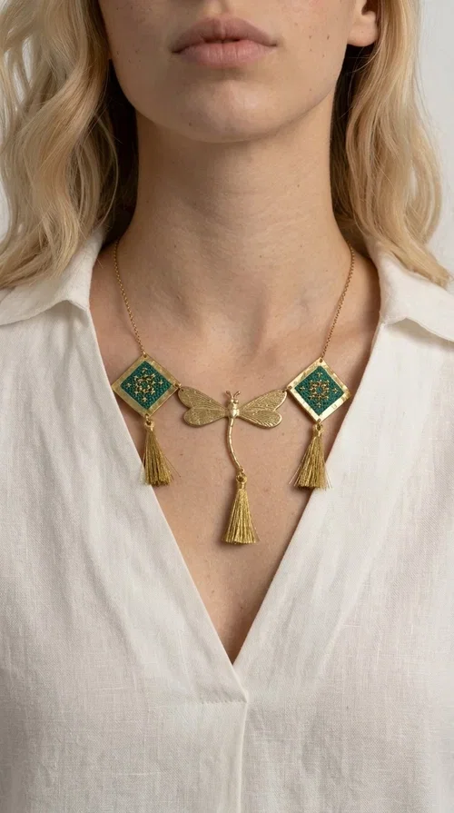 , A statement embroidered necklace that doesn't go unnoticed — featuring geometric patterns inspired by Greek tradition and a contemporary aesthetic that suits every strong feminine presence.

Designed by Greek Jewelry Designer Aikaterini Chalkiadaki, this handmade necklace combines brass and fabric in a composition strongly reminiscent of traditional folk embroidery art. Two diamond shapes of green embroidered fabric with gold geometric motifs frame a gold dragonfly at the center, while three gold tassels add movement and grace to the overall design. The result is a piece of jewelry with a deeply folklore aesthetic and, at the same time, a distinctly modern character.

Ideal for women who love striking jewelry that tells a story. It pairs perfectly with simple, monochrome looks — such as a white or cream shirt — highlighting its color and patterns. Suitable for both daytime and evening looks, receptions, weddings, or trips where you want to stand out.