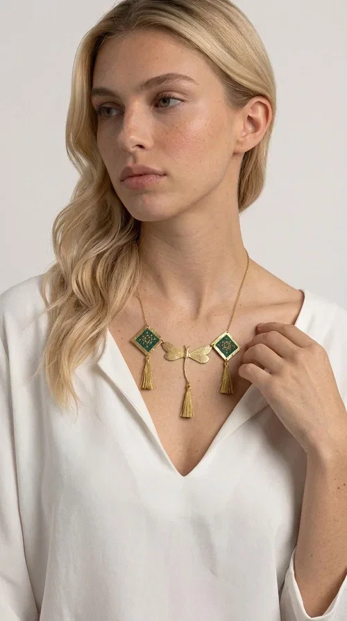 , A statement embroidered necklace that doesn't go unnoticed — featuring geometric patterns inspired by Greek tradition and a contemporary aesthetic that suits every strong feminine presence.

Designed by Greek Jewelry Designer Aikaterini Chalkiadaki, this handmade necklace combines brass and fabric in a composition strongly reminiscent of traditional folk embroidery art. Two diamond shapes of green embroidered fabric with gold geometric motifs frame a gold dragonfly at the center, while three gold tassels add movement and grace to the overall design. The result is a piece of jewelry with a deeply folklore aesthetic and, at the same time, a distinctly modern character.

Ideal for women who love striking jewelry that tells a story. It pairs perfectly with simple, monochrome looks — such as a white or cream shirt — highlighting its color and patterns. Suitable for both daytime and evening looks, receptions, weddings, or trips where you want to stand out.