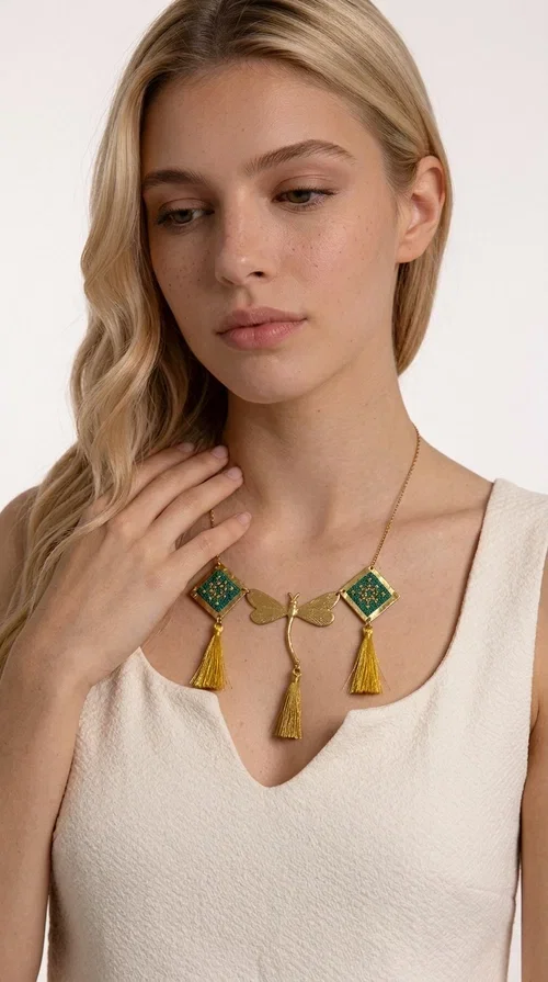 , A statement embroidered necklace that doesn't go unnoticed — featuring geometric patterns inspired by Greek tradition and a contemporary aesthetic that suits every strong feminine presence.

Designed by Greek Jewelry Designer Aikaterini Chalkiadaki, this handmade necklace combines brass and fabric in a composition strongly reminiscent of traditional folk embroidery art. Two diamond shapes of green embroidered fabric with gold geometric motifs frame a gold dragonfly at the center, while three gold tassels add movement and grace to the overall design. The result is a piece of jewelry with a deeply folklore aesthetic and, at the same time, a distinctly modern character.

Ideal for women who love striking jewelry that tells a story. It pairs perfectly with simple, monochrome looks — such as a white or cream shirt — highlighting its color and patterns. Suitable for both daytime and evening looks, receptions, weddings, or trips where you want to stand out.