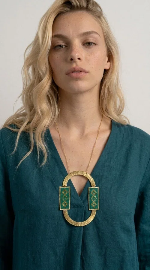 , A statement embroidered necklace that turns every look into a style declaration — featuring geometric patterns inspired by Greek folk tradition and an aesthetic that speaks for itself.

Designed by Greek Jewelry Designer Aikaterini Chalkiadaki, this long necklace combines brass and fabric in a handmade composition that highlights the art of embroidery. The oval golden brass frame embraces two rectangular fabric elements in deep green, adorned with gold-toned geometric motifs reminiscent of traditional embroidery techniques. The result is a jewelry piece with strong character, blending tradition with contemporary aesthetics.

Ideal for women who love striking jewelry, this long green necklace pairs perfectly with simple outfits — a white t-shirt, a solid-color dress, or a chic blazer. It instantly adds color, geometry, and personality to any ensemble, summer and winter alike.