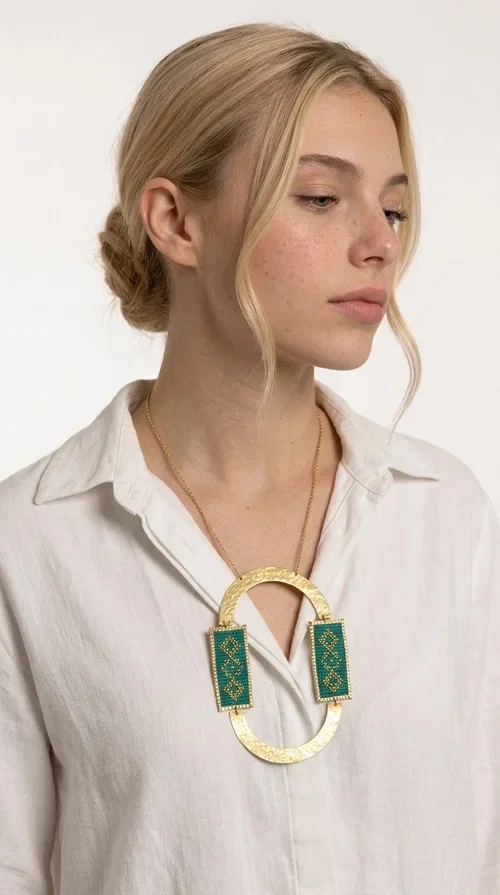 , A statement embroidered necklace that turns every look into a style declaration — featuring geometric patterns inspired by Greek folk tradition and an aesthetic that speaks for itself.

Designed by Greek Jewelry Designer Aikaterini Chalkiadaki, this long necklace combines brass and fabric in a handmade composition that highlights the art of embroidery. The oval golden brass frame embraces two rectangular fabric elements in deep green, adorned with gold-toned geometric motifs reminiscent of traditional embroidery techniques. The result is a jewelry piece with strong character, blending tradition with contemporary aesthetics.

Ideal for women who love striking jewelry, this long green necklace pairs perfectly with simple outfits — a white t-shirt, a solid-color dress, or a chic blazer. It instantly adds color, geometry, and personality to any ensemble, summer and winter alike.