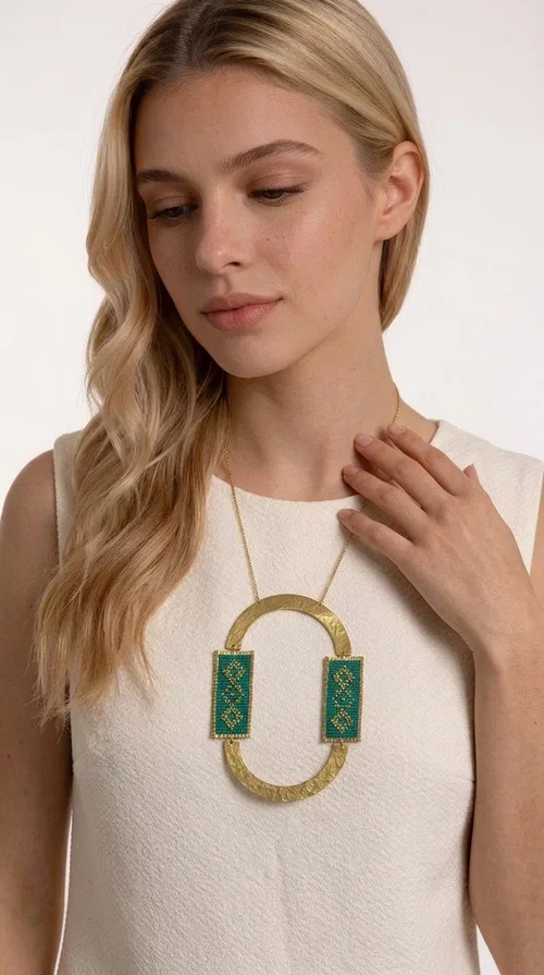 , A statement embroidered necklace that turns every look into a style declaration — featuring geometric patterns inspired by Greek folk tradition and an aesthetic that speaks for itself.

Designed by Greek Jewelry Designer Aikaterini Chalkiadaki, this long necklace combines brass and fabric in a handmade composition that highlights the art of embroidery. The oval golden brass frame embraces two rectangular fabric elements in deep green, adorned with gold-toned geometric motifs reminiscent of traditional embroidery techniques. The result is a jewelry piece with strong character, blending tradition with contemporary aesthetics.

Ideal for women who love striking jewelry, this long green necklace pairs perfectly with simple outfits — a white t-shirt, a solid-color dress, or a chic blazer. It instantly adds color, geometry, and personality to any ensemble, summer and winter alike.