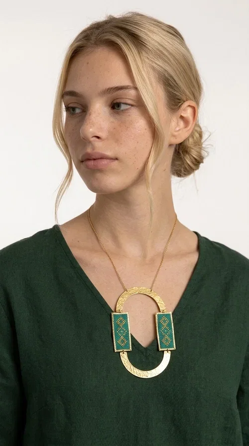 , A statement embroidered necklace that turns every look into a style declaration — featuring geometric patterns inspired by Greek folk tradition and an aesthetic that speaks for itself.

Designed by Greek Jewelry Designer Aikaterini Chalkiadaki, this long necklace combines brass and fabric in a handmade composition that highlights the art of embroidery. The oval golden brass frame embraces two rectangular fabric elements in deep green, adorned with gold-toned geometric motifs reminiscent of traditional embroidery techniques. The result is a jewelry piece with strong character, blending tradition with contemporary aesthetics.

Ideal for women who love striking jewelry, this long green necklace pairs perfectly with simple outfits — a white t-shirt, a solid-color dress, or a chic blazer. It instantly adds color, geometry, and personality to any ensemble, summer and winter alike.