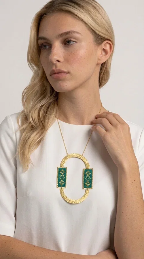 , A statement embroidered necklace that turns every look into a style declaration — featuring geometric patterns inspired by Greek folk tradition and an aesthetic that speaks for itself.

Designed by Greek Jewelry Designer Aikaterini Chalkiadaki, this long necklace combines brass and fabric in a handmade composition that highlights the art of embroidery. The oval golden brass frame embraces two rectangular fabric elements in deep green, adorned with gold-toned geometric motifs reminiscent of traditional embroidery techniques. The result is a jewelry piece with strong character, blending tradition with contemporary aesthetics.

Ideal for women who love striking jewelry, this long green necklace pairs perfectly with simple outfits — a white t-shirt, a solid-color dress, or a chic blazer. It instantly adds color, geometry, and personality to any ensemble, summer and winter alike.