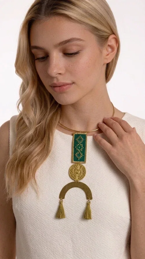 , A statement embroidered necklace that instantly catches the eye — featuring a bold green color, geometric patterns and gold details reminiscent of the tradition of folk jewelry.

Designed by Greek Jewelry Designer Aikaterini Chalkiadaki, this handmade necklace combines brass and fabric in a composition that highlights the skill of Greek craftsmanship. The rectangular embroidered piece, with its delicate geometric motifs in gold and green tones, blends harmoniously with a gold circular disc and a brass arc, while three hanging tassels in a khaki-gold shade add movement and warmth to the overall look. It is worn on a gold rigid choker for an even more striking effect.

Ideal for looks that want to stand out — from summer evening outings to casual chic styles with simple linen or cotton clothing. It pairs perfectly with neutral tones, white, ecru, or deep green shades.