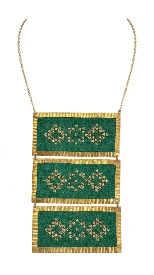 , An embroidered green necklace that blends tradition with contemporary design — ideal for those who want to make a statement in a truly unique way. Designed by Greek Jewelry Designer Aikaterini Chalkiadaki, this striking necklace brings a breath of fresh air to the world of handmade jewelry. The deep green fabric combined with golden geometric embroidered motifs creates a sense of richness and authenticity rarely found in mass-produced jewelry.

The necklace is made of three rectangular brass sections, covered in green fabric and adorned with embroidered geometric patterns inspired by Greek folk tradition (folklore). The delicate gold chain that accompanies it adds grace and balance, making it ideal for both daytime looks and evening outings. It pairs perfectly with white, ecru, or monochrome outfits, instantly adding character to any look.