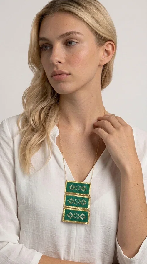 , An embroidered green necklace that blends tradition with contemporary design — ideal for those who want to make a statement in a truly unique way. Designed by Greek Jewelry Designer Aikaterini Chalkiadaki, this striking necklace brings a breath of fresh air to the world of handmade jewelry. The deep green fabric combined with golden geometric embroidered motifs creates a sense of richness and authenticity rarely found in mass-produced jewelry.

The necklace is made of three rectangular brass sections, covered in green fabric and adorned with embroidered geometric patterns inspired by Greek folk tradition (folklore). The delicate gold chain that accompanies it adds grace and balance, making it ideal for both daytime looks and evening outings. It pairs perfectly with white, ecru, or monochrome outfits, instantly adding character to any look.
