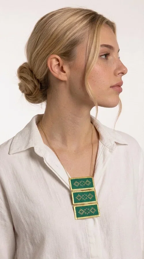 , An embroidered green necklace that blends tradition with contemporary design — ideal for those who want to make a statement in a truly unique way. Designed by Greek Jewelry Designer Aikaterini Chalkiadaki, this striking necklace brings a breath of fresh air to the world of handmade jewelry. The deep green fabric combined with golden geometric embroidered motifs creates a sense of richness and authenticity rarely found in mass-produced jewelry.

The necklace is made of three rectangular brass sections, covered in green fabric and adorned with embroidered geometric patterns inspired by Greek folk tradition (folklore). The delicate gold chain that accompanies it adds grace and balance, making it ideal for both daytime looks and evening outings. It pairs perfectly with white, ecru, or monochrome outfits, instantly adding character to any look.