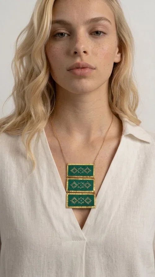 , An embroidered green necklace that blends tradition with contemporary design — ideal for those who want to make a statement in a truly unique way. Designed by Greek Jewelry Designer Aikaterini Chalkiadaki, this striking necklace brings a breath of fresh air to the world of handmade jewelry. The deep green fabric combined with golden geometric embroidered motifs creates a sense of richness and authenticity rarely found in mass-produced jewelry.

The necklace is made of three rectangular brass sections, covered in green fabric and adorned with embroidered geometric patterns inspired by Greek folk tradition (folklore). The delicate gold chain that accompanies it adds grace and balance, making it ideal for both daytime looks and evening outings. It pairs perfectly with white, ecru, or monochrome outfits, instantly adding character to any look.