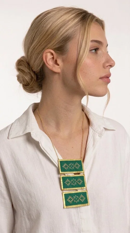 , An embroidered green necklace that blends tradition with contemporary design — ideal for those who want to make a statement in a truly unique way. Designed by Greek Jewelry Designer Aikaterini Chalkiadaki, this striking necklace brings a breath of fresh air to the world of handmade jewelry. The deep green fabric combined with golden geometric embroidered motifs creates a sense of richness and authenticity rarely found in mass-produced jewelry.

The necklace is made of three rectangular brass sections, covered in green fabric and adorned with embroidered geometric patterns inspired by Greek folk tradition (folklore). The delicate gold chain that accompanies it adds grace and balance, making it ideal for both daytime looks and evening outings. It pairs perfectly with white, ecru, or monochrome outfits, instantly adding character to any look.