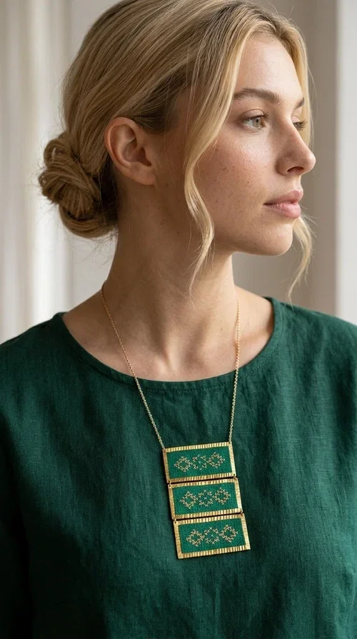 , An embroidered green necklace that blends tradition with contemporary design — ideal for those who want to make a statement in a truly unique way. Designed by Greek Jewelry Designer Aikaterini Chalkiadaki, this striking necklace brings a breath of fresh air to the world of handmade jewelry. The deep green fabric combined with golden geometric embroidered motifs creates a sense of richness and authenticity rarely found in mass-produced jewelry.

The necklace is made of three rectangular brass sections, covered in green fabric and adorned with embroidered geometric patterns inspired by Greek folk tradition (folklore). The delicate gold chain that accompanies it adds grace and balance, making it ideal for both daytime looks and evening outings. It pairs perfectly with white, ecru, or monochrome outfits, instantly adding character to any look.