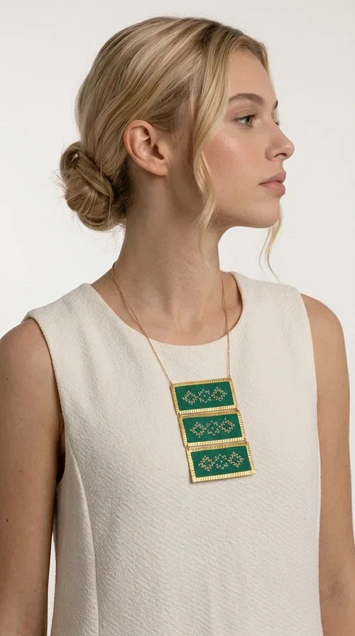, An embroidered green necklace that blends tradition with contemporary design — ideal for those who want to make a statement in a truly unique way. Designed by Greek Jewelry Designer Aikaterini Chalkiadaki, this striking necklace brings a breath of fresh air to the world of handmade jewelry. The deep green fabric combined with golden geometric embroidered motifs creates a sense of richness and authenticity rarely found in mass-produced jewelry.

The necklace is made of three rectangular brass sections, covered in green fabric and adorned with embroidered geometric patterns inspired by Greek folk tradition (folklore). The delicate gold chain that accompanies it adds grace and balance, making it ideal for both daytime looks and evening outings. It pairs perfectly with white, ecru, or monochrome outfits, instantly adding character to any look.
