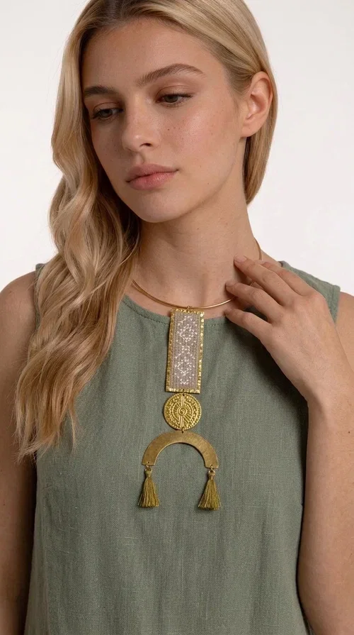 , A statement embroidered necklace that instantly catches the eye — featuring ivory geometric patterns on a brass frame, with details inspired by folklore tradition. Designed by Greek Jewelry Designer Aikaterini Chalkiadaki, this handmade necklace combines the art of embroidery with a modern aesthetic, creating a truly distinctive piece.

The necklace features a rectangular embroidered panel with delicate geometric motifs in shades of ivory and gold, a circular brass element with an embossed design at the center, and a semicircular base adorned with two gold tassels that add movement and a luxurious feel. The brass neck ring ensures a secure fit and timeless style.

Ideal for women who love striking jewelry with character, it pairs beautifully with simple ivory or white outfits, as well as bold colors for contrast. Perfect for evening outings, summer events, weddings, or stylish daytime looks.