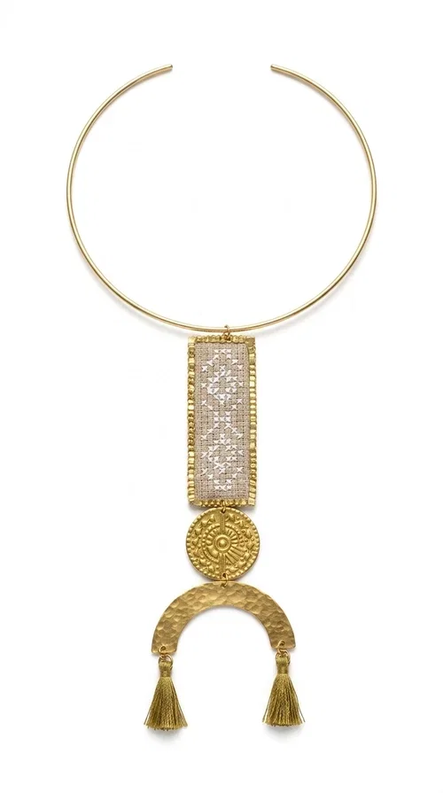 , A statement embroidered necklace that instantly catches the eye — featuring ivory geometric patterns on a brass frame, with details inspired by folklore tradition. Designed by Greek Jewelry Designer Aikaterini Chalkiadaki, this handmade necklace combines the art of embroidery with a modern aesthetic, creating a truly distinctive piece.

The necklace features a rectangular embroidered panel with delicate geometric motifs in shades of ivory and gold, a circular brass element with an embossed design at the center, and a semicircular base adorned with two gold tassels that add movement and a luxurious feel. The brass neck ring ensures a secure fit and timeless style.

Ideal for women who love striking jewelry with character, it pairs beautifully with simple ivory or white outfits, as well as bold colors for contrast. Perfect for evening outings, summer events, weddings, or stylish daytime looks.