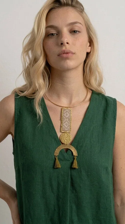 , A statement embroidered necklace that instantly catches the eye — featuring ivory geometric patterns on a brass frame, with details inspired by folklore tradition. Designed by Greek Jewelry Designer Aikaterini Chalkiadaki, this handmade necklace combines the art of embroidery with a modern aesthetic, creating a truly distinctive piece.

The necklace features a rectangular embroidered panel with delicate geometric motifs in shades of ivory and gold, a circular brass element with an embossed design at the center, and a semicircular base adorned with two gold tassels that add movement and a luxurious feel. The brass neck ring ensures a secure fit and timeless style.

Ideal for women who love striking jewelry with character, it pairs beautifully with simple ivory or white outfits, as well as bold colors for contrast. Perfect for evening outings, summer events, weddings, or stylish daytime looks.