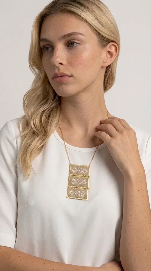 , The statement embroidered ivory necklace is a handmade creation that combines the traditional art of embroidery with a contemporary jewelry aesthetic, adding a unique, eye-catching touch to any outfit.

Designed by Greek Jewelry Designer Aikaterini Chalkiadaki, this necklace features three rectangular embroidered sections with ivory geometric motifs and gold details set in a brass frame. It hangs from a delicate gold chain that lends elegance and lightness, while the folklore-style geometric patterns give the piece a distinctive, ethnographic character. The combination of brass and fabric creates an intriguing contrast of materials that draws the eye.

Ideal for both day and evening wear, it pairs beautifully with white or monochrome outfits to highlight its geometric patterns. The ivory color makes it versatile and timeless, perfect for summer looks as well as formal or business occasions.