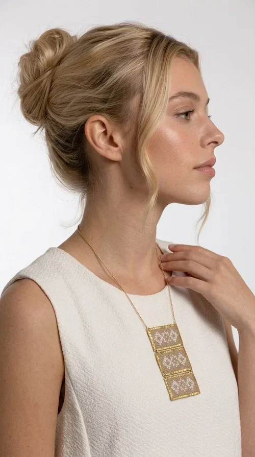 , The statement embroidered ivory necklace is a handmade creation that combines the traditional art of embroidery with a contemporary jewelry aesthetic, adding a unique, eye-catching touch to any outfit.

Designed by Greek Jewelry Designer Aikaterini Chalkiadaki, this necklace features three rectangular embroidered sections with ivory geometric motifs and gold details set in a brass frame. It hangs from a delicate gold chain that lends elegance and lightness, while the folklore-style geometric patterns give the piece a distinctive, ethnographic character. The combination of brass and fabric creates an intriguing contrast of materials that draws the eye.

Ideal for both day and evening wear, it pairs beautifully with white or monochrome outfits to highlight its geometric patterns. The ivory color makes it versatile and timeless, perfect for summer looks as well as formal or business occasions.